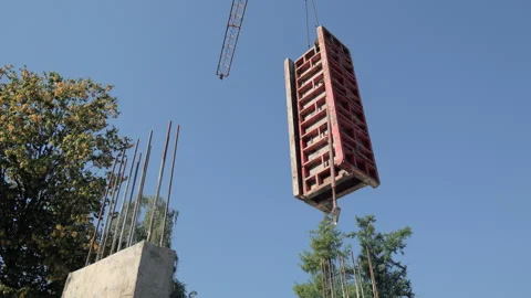 Large red formwork panel lifted by crane at construction site, concrete columns Stock Footage 317881975