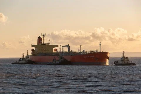 A large red oil tanker ship with tugs near sunset Stock Photos