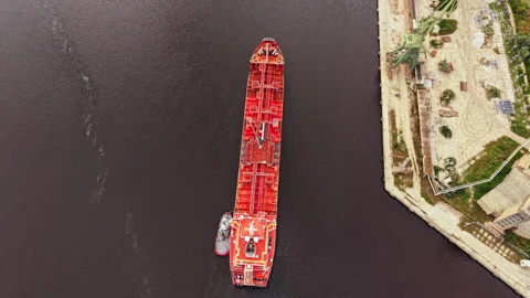 Large red ship navigating through water near a dock in an industrial area during Stock Footage 340882821