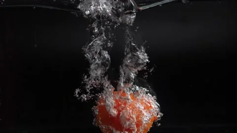 A large red tomato falls into the water with splashes, slowly sinking to the bot Stock Footage 133354489