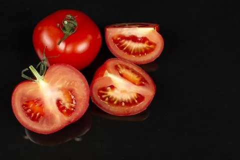 Large red tomatoes and cut halves on a black background Foto stock