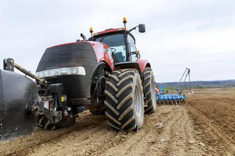 A large red tractor close-up with sowing equipment stands in a field. Stock Photos