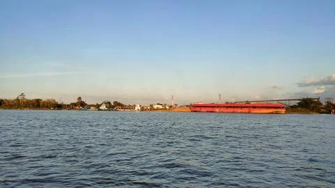 A large river with a coal cargo ship visible in the distance during the day. Stock Photos