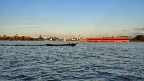 A large river with a coal cargo ship visible in the distance during the day. Stock Photos