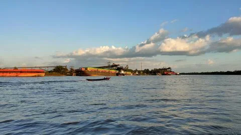 A large river with a coal cargo ship visible in the distance during the day. Stock Photos