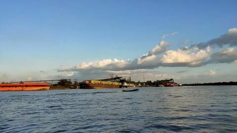 A large river with a coal cargo ship visible in the distance during the day. Stock Photos