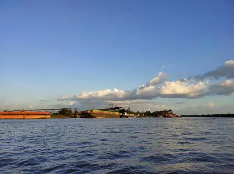 A large river with a coal cargo ship visible in the distance during the day. Stock Photos