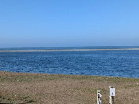 A large river flows toward the vast ocean beneath a clear blue sky Stockfoto's