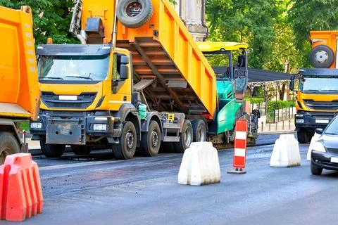 Large road construction equipment is actively working on the city street, l.. Stock Photos