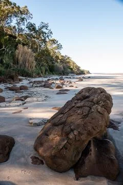 A large rock sits on a beach, surrounded by small rocks Foto stock