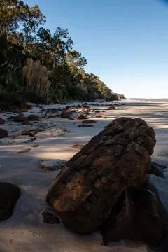 A large rock sits on a beach, surrounded by small rocks Stock Photos