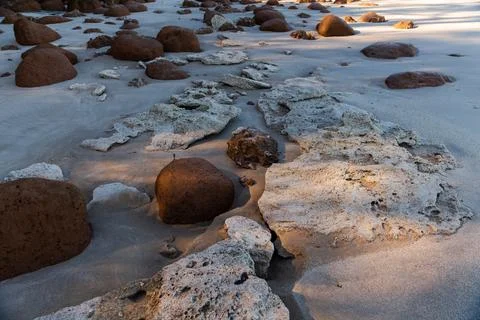 A large rock sits on a beach, surrounded by small rocks Foto stock