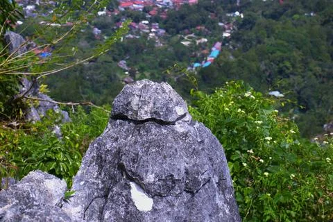 A large rock sits on a hillside with a view of a city below Stock Photos