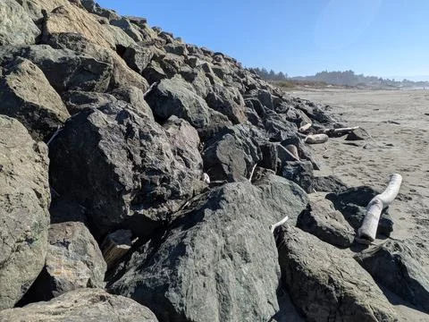 Large rocks form a rugged hillside leading to a sandy beach Stock Photos