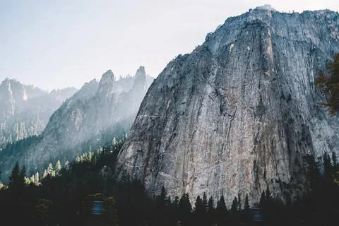 Large rocky mountain with forest at base and cloudy sky Foto stock