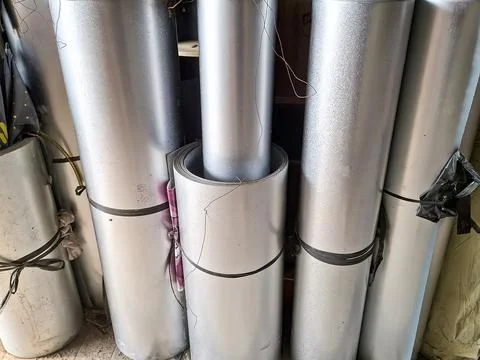 Large rolls of shiny galvanized sheet metal stored vertically in a workshop.. Stock Photos