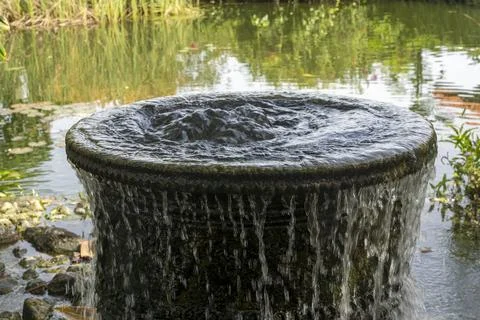Large, round, black container with water pouring out of it Stock Photos