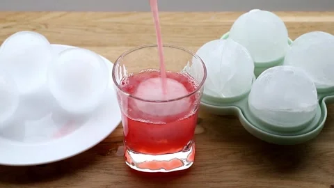 A large round ice cube in a glass, with a drink being poured. Stock Footage 340147148