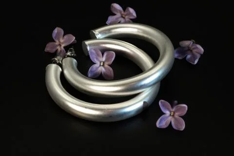 Large round metallic silver earrings and lilac flowers. Stock Photos