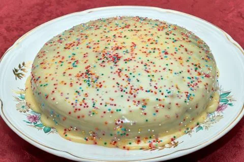 A large round sponge cake with custard, decorated with small colored balls. Stock Photos