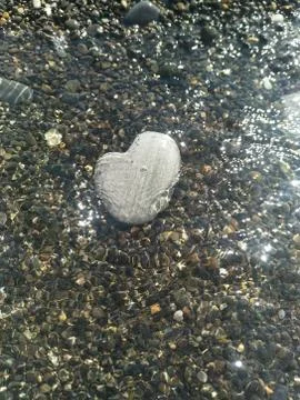 Large rounded light grey stone in shape of heart lies under the water near th Stock Photos