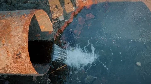 A large rusty metal pipe through which chemical waste is dumped into the rive Stock Footage 245476251