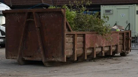 Large rusty metal roll off skip bin filled with garden green waste tree branc Fotos Stock