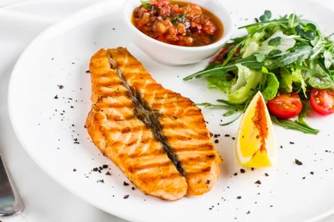 The large salmon steak red fish on the grill with lemon, sauce with vegetable Stock Photos