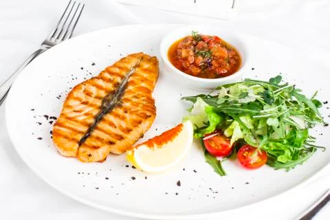 The large salmon steak red fish on the grill with lemon, sauce with vegetable Stock Photos