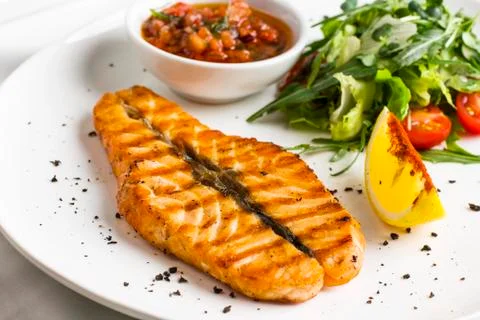 The large salmon steak red fish on the grill with lemon, sauce with vegetable Stock Photos