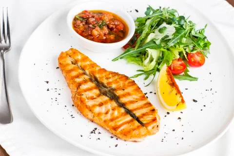 The large salmon steak red fish on the grill with lemon, sauce with vegetable Stock Photos