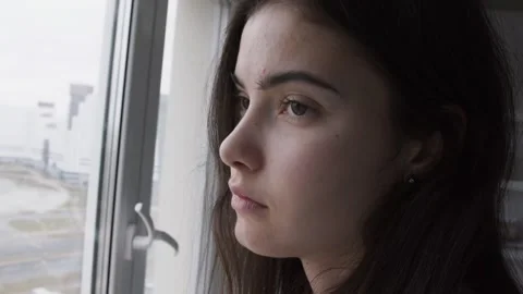 Large scale close up portrait of unhappy cute girl looking through window glass Video stock 165155484