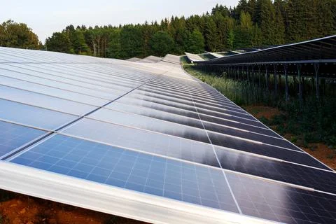 Large scale solar panels array stretching across hills near a green forest, r Stock Photos