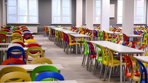 A large school cafeteria with long rows of tables and colorful chairs. Video stock 331205869