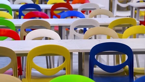 A large school cafeteria with long rows of tables and colorful chairs. Vídeo Stock 340065621