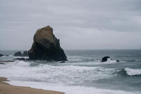Large sea stack rising from waves on overcast day in Santa Cruz Portugal Foto stock