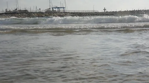 Large sea waves with splashes of foam and water on the beach with yacht port Видео 92574765