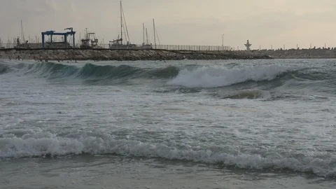 Large sea waves with splashes of foam and water on the beach with yacht port Stock Footage 93555525