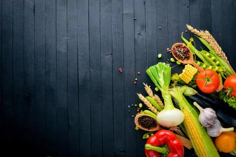 A large selection of raw fresh vegetables and spices. On a black wooden backg Stock Photos