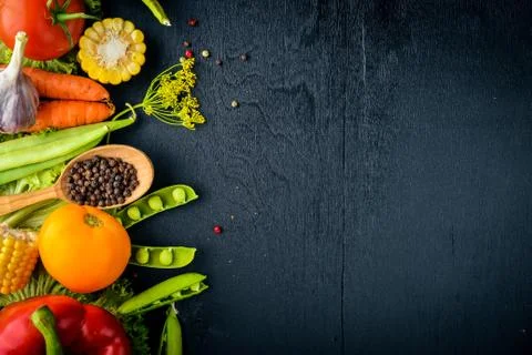 A large selection of raw fresh vegetables and spices. On a black wooden backg Stock Photos