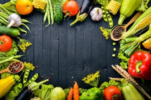 A large selection of raw fresh vegetables and spices. On a black wooden backg Stock Photos