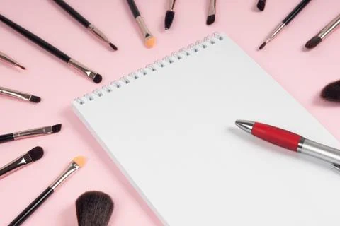 Large set of makeup brushes with a notebook and pen mock-up on a pink backgro Stock Photos