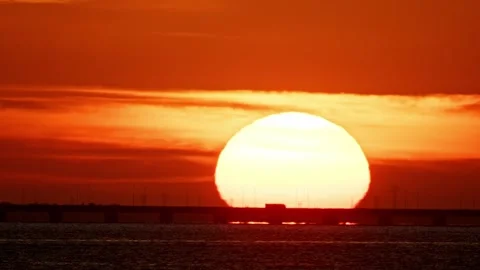 Large setting sun over calm ocean and bridge Stock Footage 309815953