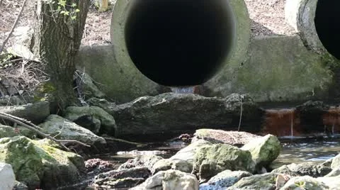 Large sewer drain pipe with water flowing out of it into a contamiated stream 動画素材 10842458