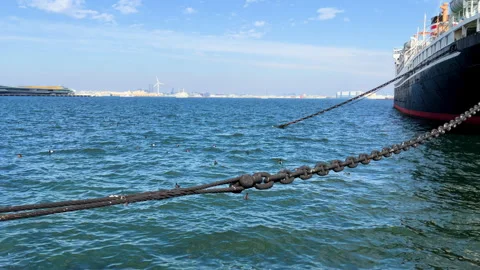 Large ship moored to a dock using a heavy chain, with the ocean a city skyline Stock-Footage 258414969