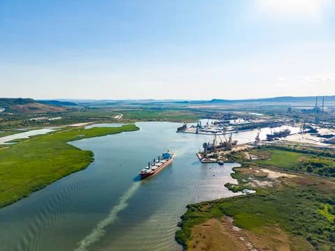Large ship moves along the river past industrial area with cranes under a c.. Stock Photos