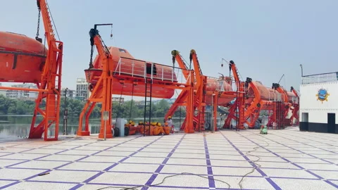Large ship with multiple orange lifeboats and cranes. lifeboat is being lowered Stock Footage 296320449