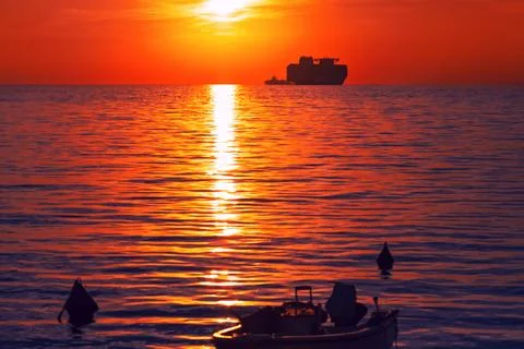 Large ship rests on horizon while small boat floats in foreground Stock-Fotos