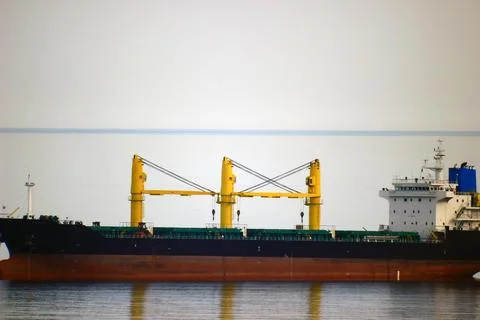 A large ship with yellow cranes is reflected in sea water 스톡 사진