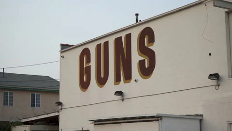 A Large Sign On The Side Of A Gun Store That Simply Says "GUNS" Stock Footage 139426360